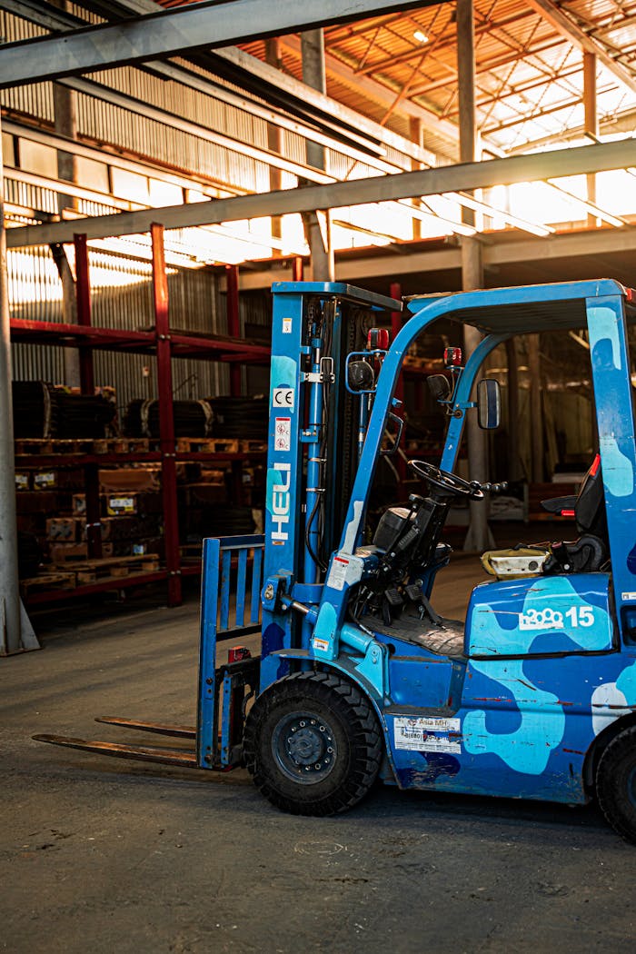 A vividly colored blue forklift parked in a well-lit, spacious warehouse with metal shelving in the background.
